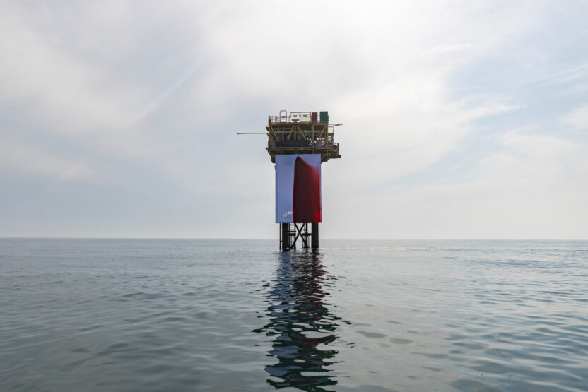 Fake blood stains a giant white fabric backdrop attached to an offshore platform in a calm ocean.