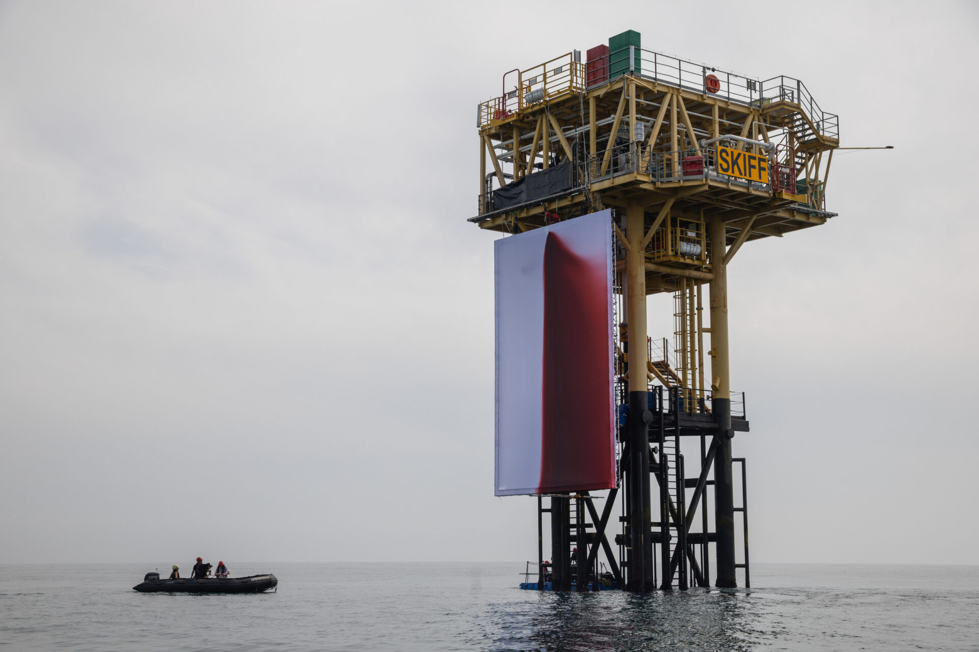 Fake blood stains a giant white fabric backdrop attached to an offshore platform in a calm ocean.