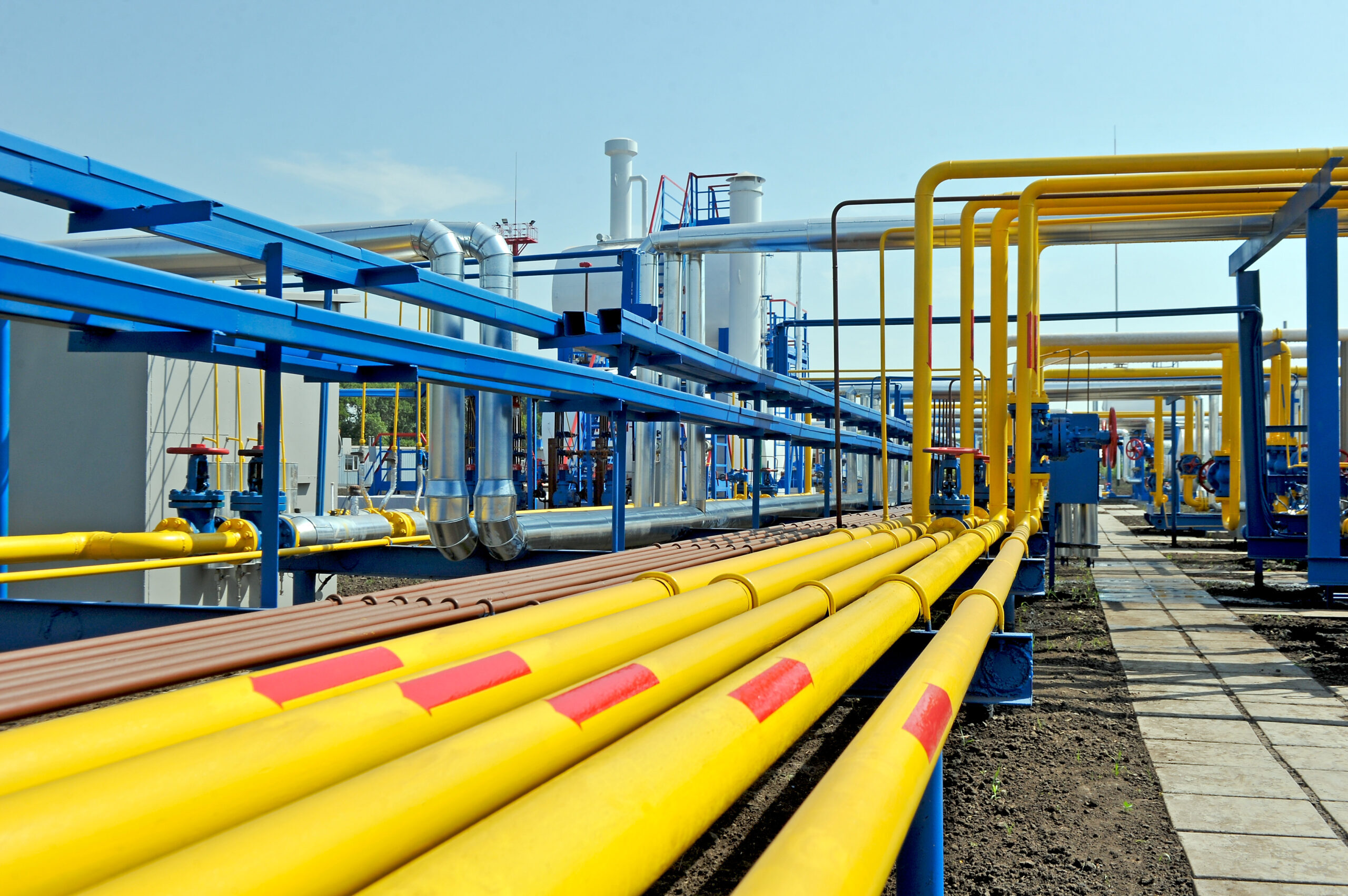 A network of yellow and blue pipes at a gas facility under a clear sky.