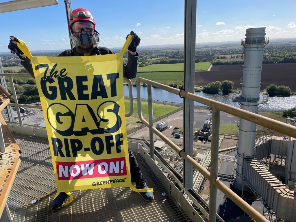 Activist on a metal gantry high in the air holding a banner reading 'The Great Gas Rip-Off Now On'