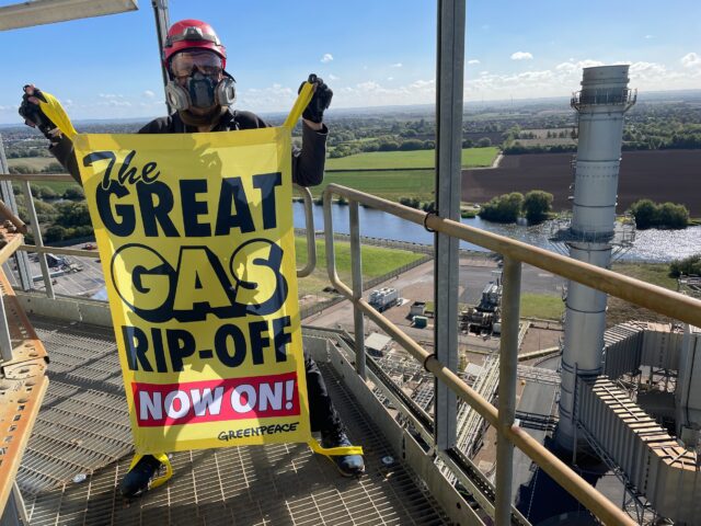 Activist on a metal gantry high in the air holding a banner reading 'The Great Gas Rip-Off Now On'